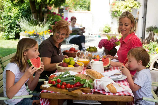 Family enjoying  a balanced no-cook summer meal with fresh fruits, vegetables, cheese and whole grain foods outdoors